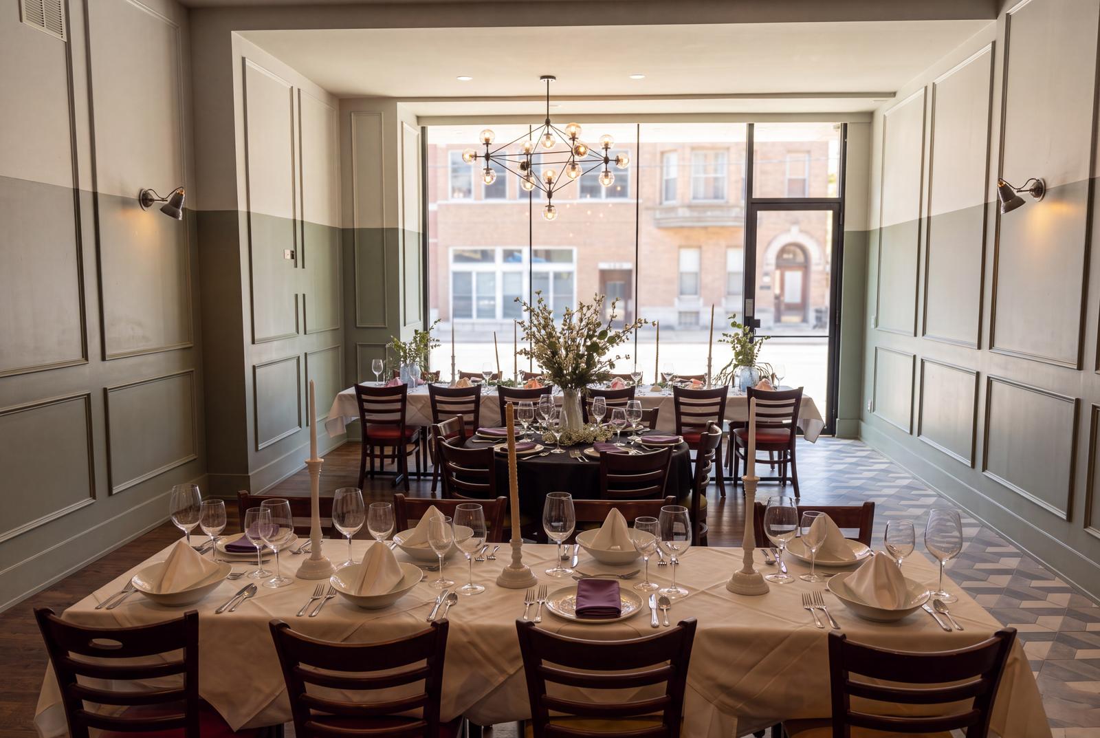 A long dinner table under the chandelier by the front windows