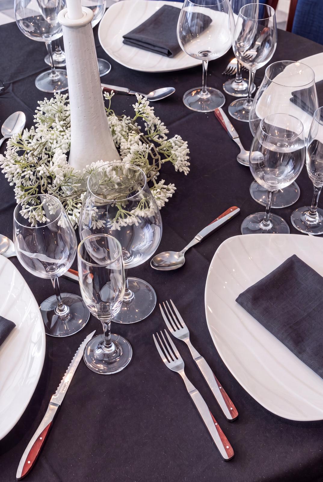 A place setting with black linen, crystal and a white floral centerpiece