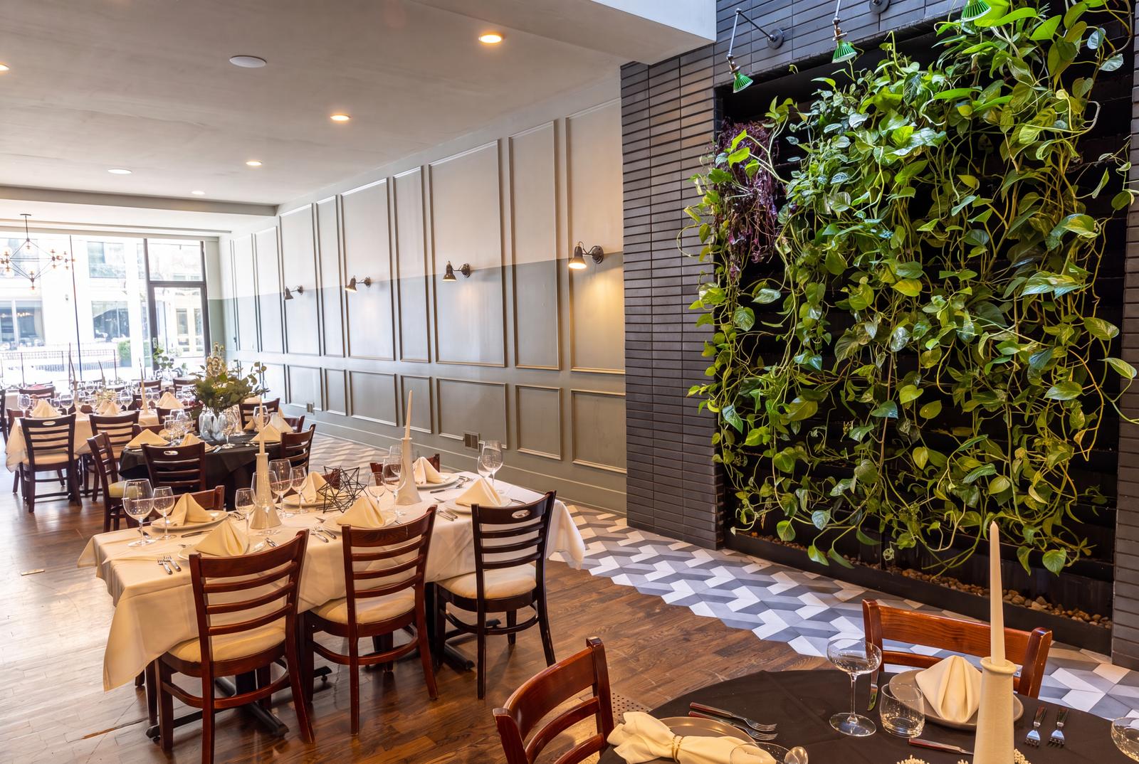Sala set for a dinner party, with sage-green paneled walls, a living plant wall and tables dressed in white linen