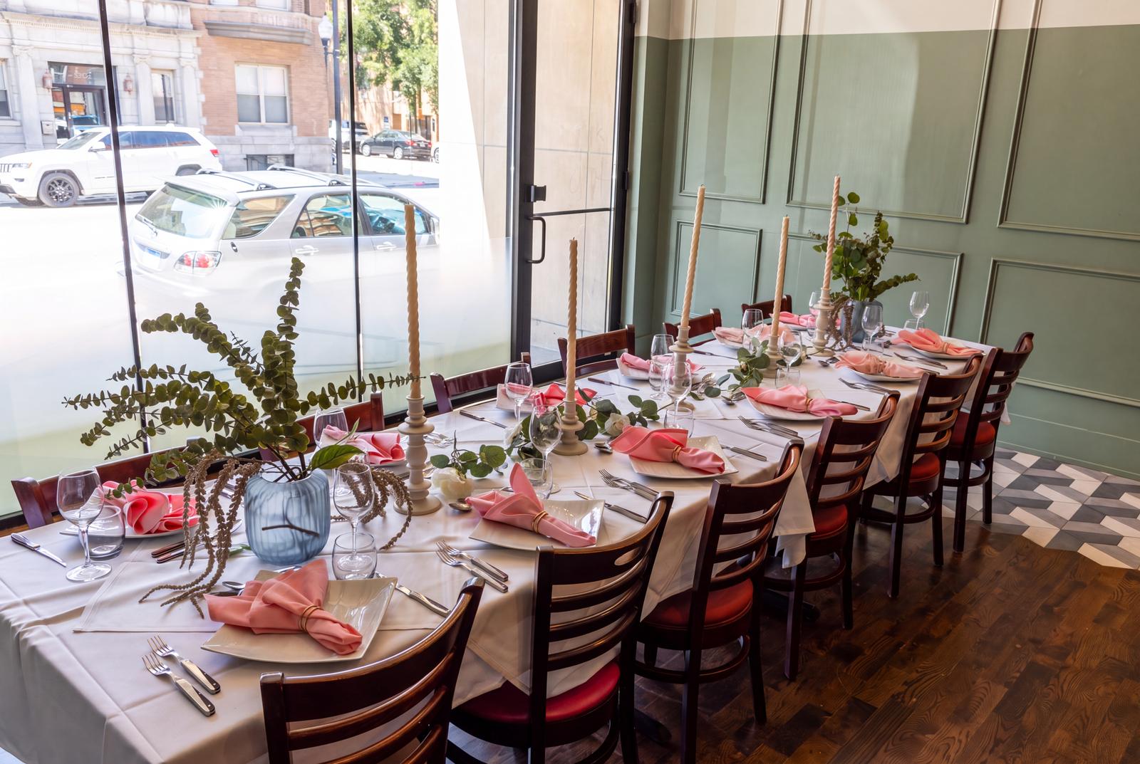 A table by the window dressed with pink napkins and greenery